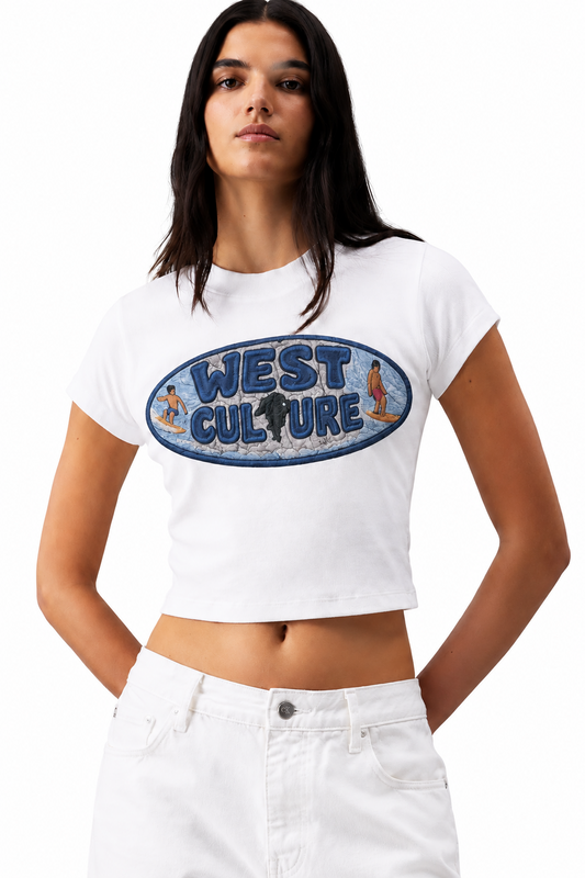 A woman modeling a white cropped t-shirt with a blue 'West Culture' graphic on the chest, paired with white jeans, against a solid gray studio background.